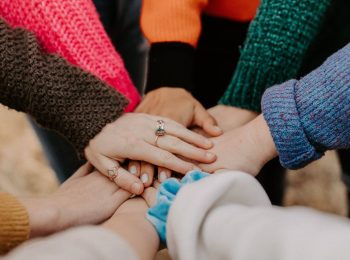 image of multiple individuals placing their arms in the center, with hands overlapping as a sign of friendship.