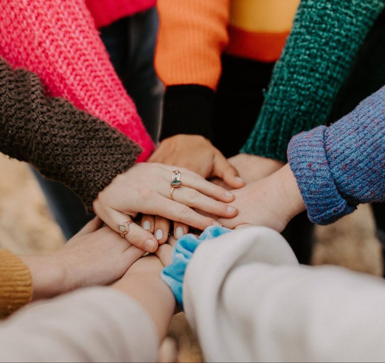 image of multiple individuals placing their arms in the center, with hands overlapping as a sign of friendship.